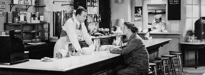 szene aus stummfilm: mann sitzt am barhocker und bestellt beim barkeeper