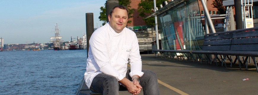 Foto von Martin Kirchgasser, neuer Küchenchef im Westin Hamburg in der Elbphilharmonie, sitzt auf einem Pfeiler am Hamburger Hafen.