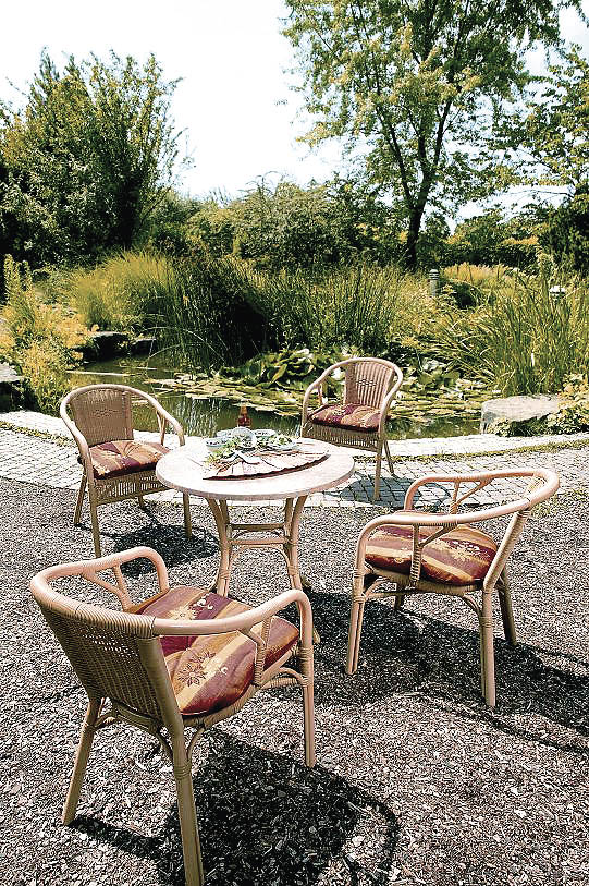Ein Bistrotisch mit Sesseln aus Rattan Textur neben einem Teich in der Sonne 