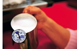 eine Hand haelt den Milchschaeumer mit dem Thermometer, welches die richtige Temperatur anzeigt 