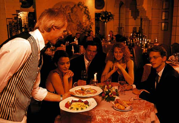 zwei Paare beim Abendessen, während der Kellner die Gerichte serviert 