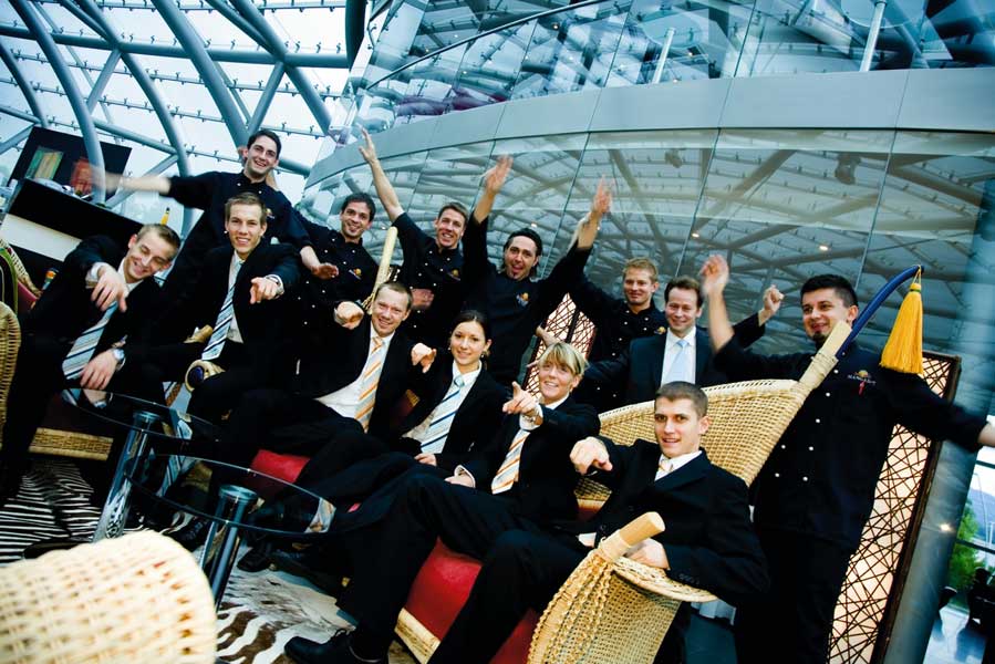 die Crew des Hangar 7 in Anzügen sitzend und lächelnd 