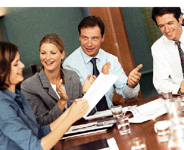 ein geschäftsmeeting ist zu sehen, zwei frauen und zwei herren sitzen an einem konferenztisch,die dame hält notizen in der hand während die anderen drei menschen applaudieren 