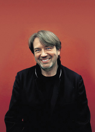 Klaus Kobjoll vor einem roten Hintergrund in schwarzer Kleidung 