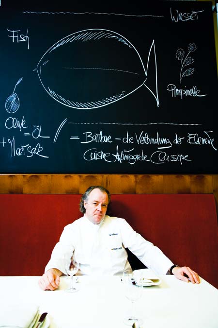 Michael Hoffmann sitzt in seinem Restaurant vor einer gewaltigen Kreidetafel an der Wand 