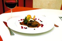 ein gedeckter Tisch, ein Glas Rotwein und eine Wildkreation auf dem Teller 