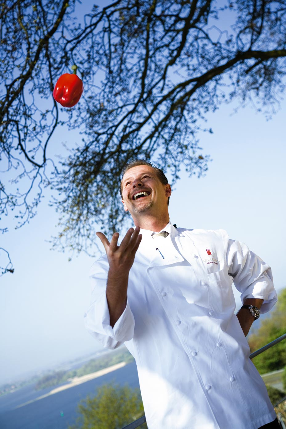 Karlheinz Hauser steht im Grünen und wirft roten Paprika in die Luft 
