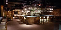 eine Bar aus Holz ist zu sehen, darum befinden sich Esstische mit freistehenden Stühlen 
