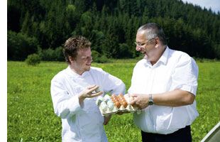 Gerhard Fuchs mit freilandeiern in der hand waehrend er sich mit einem zweiten mann unterhaelt 