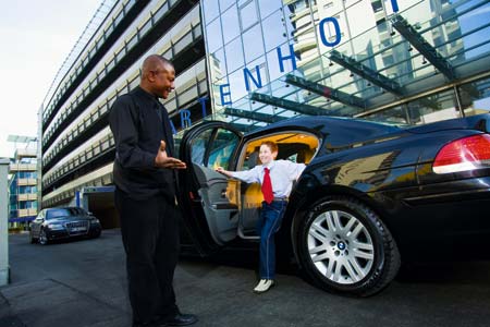 ein Herr öffnet die hintere Türe des Wagens, es steigt ein gut gelauntes Kind aus