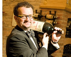 Alexander Adlgasser trägt eine Magnum Flasche Wein auf der Schulter 