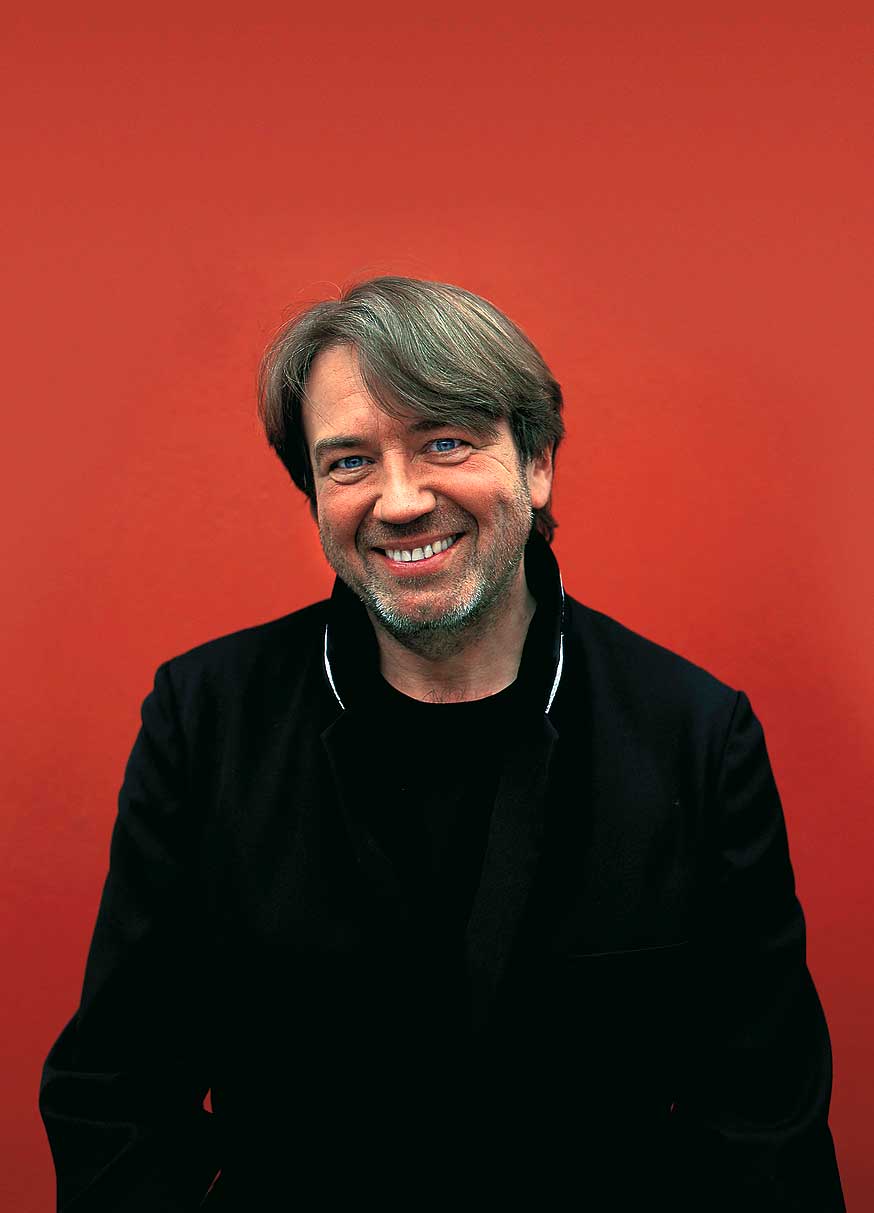 klaus kobjoll in seiner Uniform lächelnd vor einem roten Hintergrund 