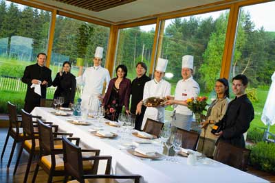 das Küchen und Gastropersonal posiert vor einem riesengroßen Panoramafenster und vor einer langen weißgedeckten Tafel 