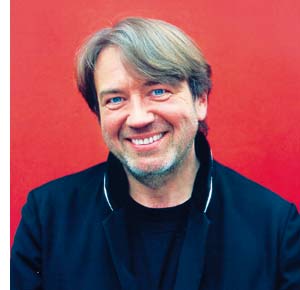 ein Mittelalter Herr mit einem symphatischen Lächeln sitzend vor einer roten Wand