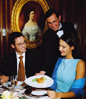 ein Liebespaar sitzt im Restaurant, der Kellner bringt der Dame ihr Gericht. Alle lächeln 