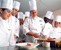 das Küchenteam sieht dem Meister bei der Arbeit zu, alle sind um den Koch versammelt, 