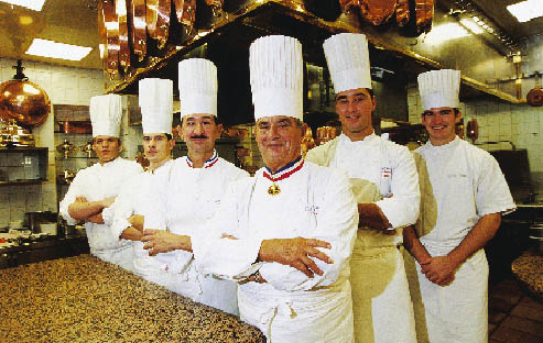 Paul Bocuse und Crew die Arme verschränkt und in der typischen Kochuniform 