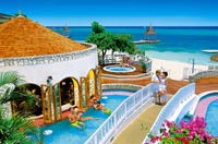Die Poollandschaft der Hotelanlage direkt am Strand ist zu sehen, auf der kleinen Brücke über dem Pool ist ein Liebespaar zu sehen