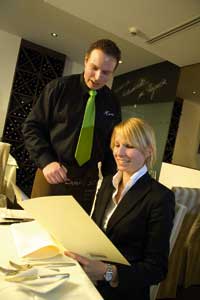 eine Dame im Blazer und ein Herr in Hemd und Krawatte besprechen eventuell die Weinkarte 