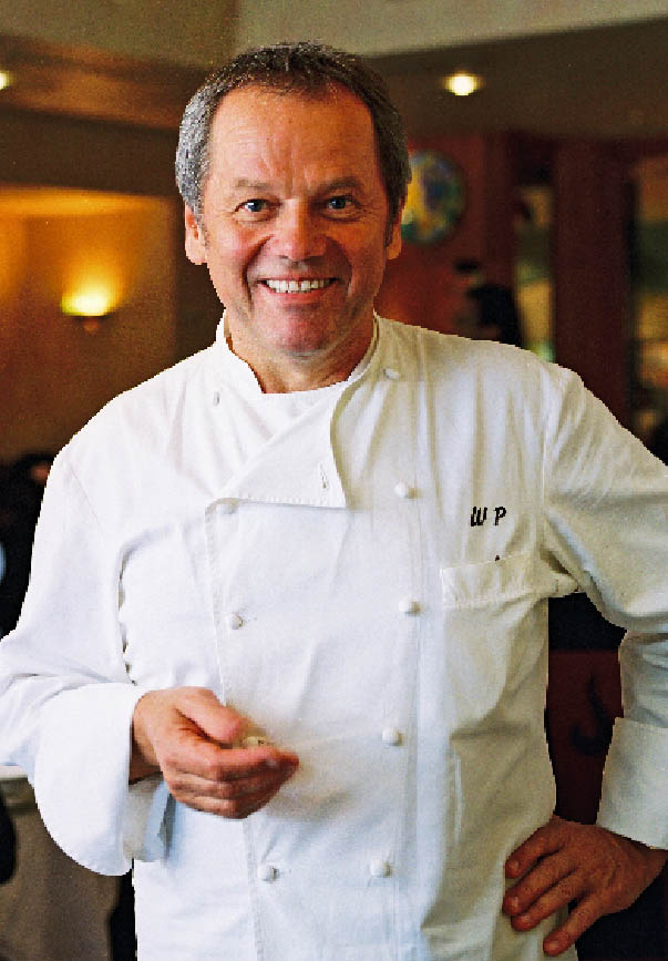 Wolfgang Puck in weißer Kochjacke, auf der Brust seine Initalien 