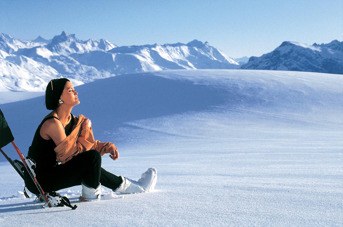 Wintersaison Eine Frau sitzt auf einem von Schnee bedecktem Berg und genießt die Sonnenstrahlen
