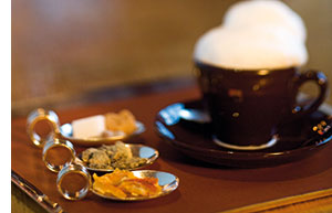 eine Tasse Kaffee mit Milchschaum und drei Loeffel mit Zucker und Sueskram 