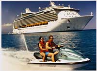 ein Paar fährt Jet-Ski während im Hintergrund ein Kreuzfahrtschiff zu sehen ist 