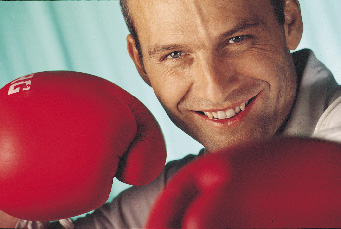 Ein Mann mit roten boxhandschuhen, in verteidungshaltung lächelt in die kamera 