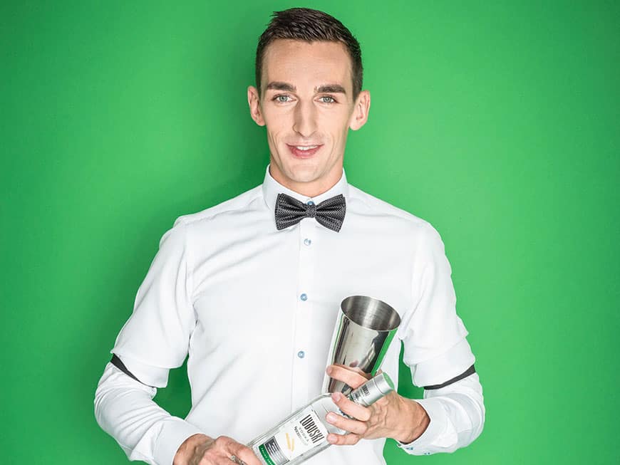 Posłuszny: „Der perfekte Drink ist immer von der Gemütslage und Atmosphäre abhängig.“ Bartender Marek Posłuszny mit Flasche vor grünem Hintergrund