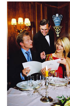 Ein Paar bei einem romantischen Abendessen bei Kerzenschein wird vom Kellner beraten 
