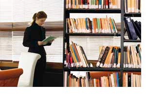 eine Frau neben einem Bücherregal, stehend und lesend 