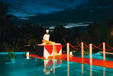eine bruecke mit rotem teppich ueber den hotelpool gelegt, am ende befindet sich ein mitarbeiter hinter einem buffetttisch 