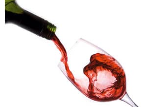 ein Flaschenhals ist zu sehen, es wird gerade Rotwein aus der Flasche in ein Glas gefuellt 
