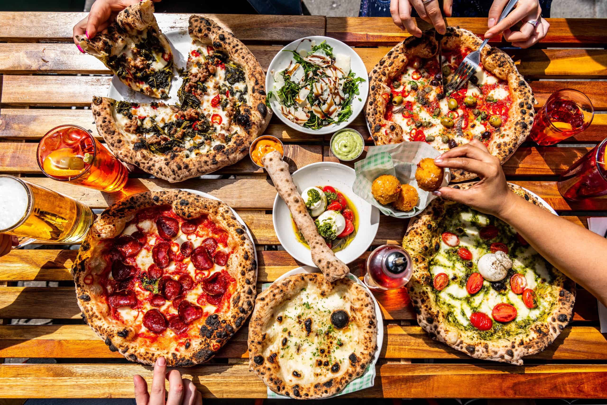 Verschiedene neapolitanische Pizzen, Salat, Snacks und Getränke von Pizza Pilgrims auf einem Holztisch.