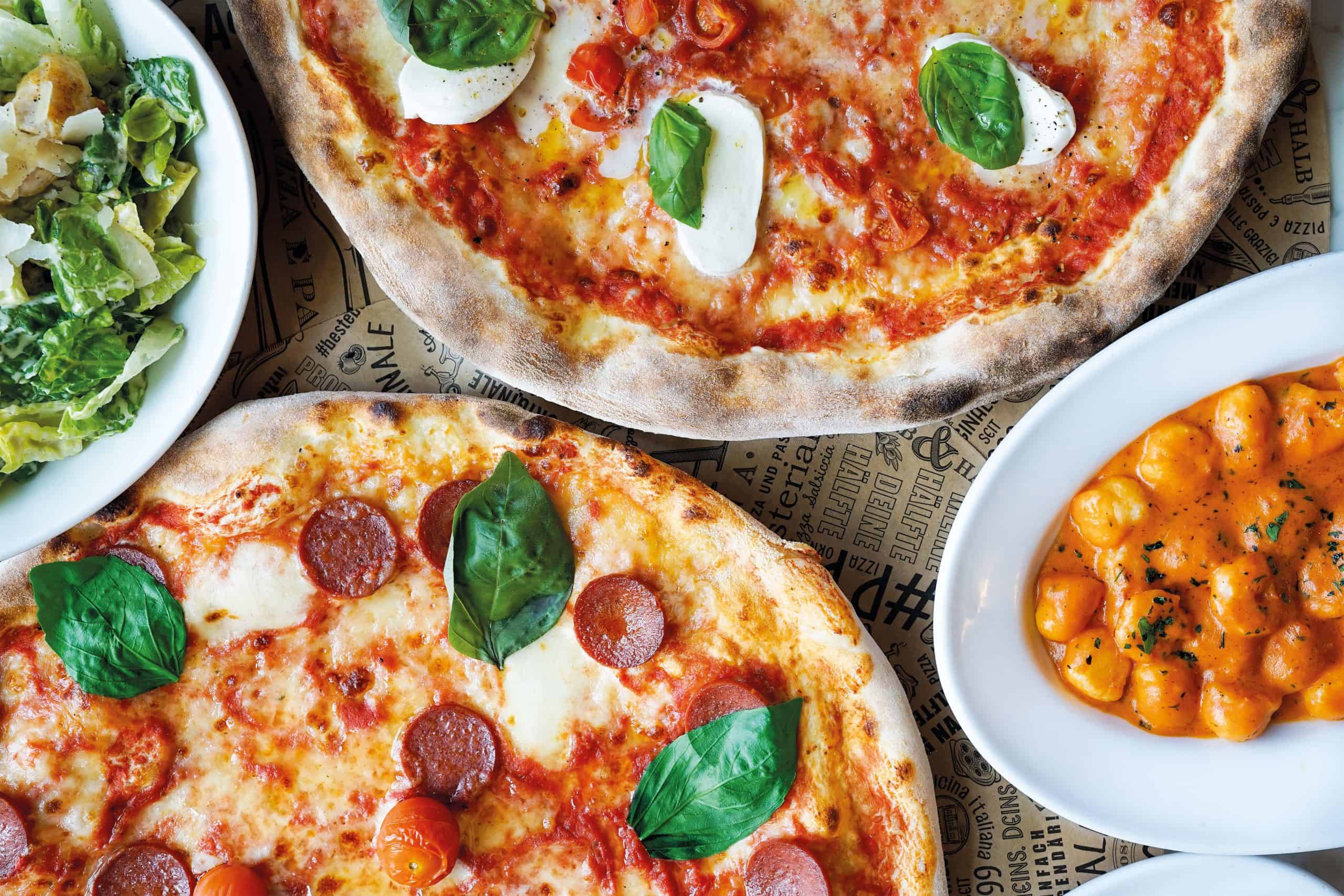 Zwei Pizzen mit Mozzarella und Basilikum neben Salat und Gnocchi in Sauce bei L’Osteria.