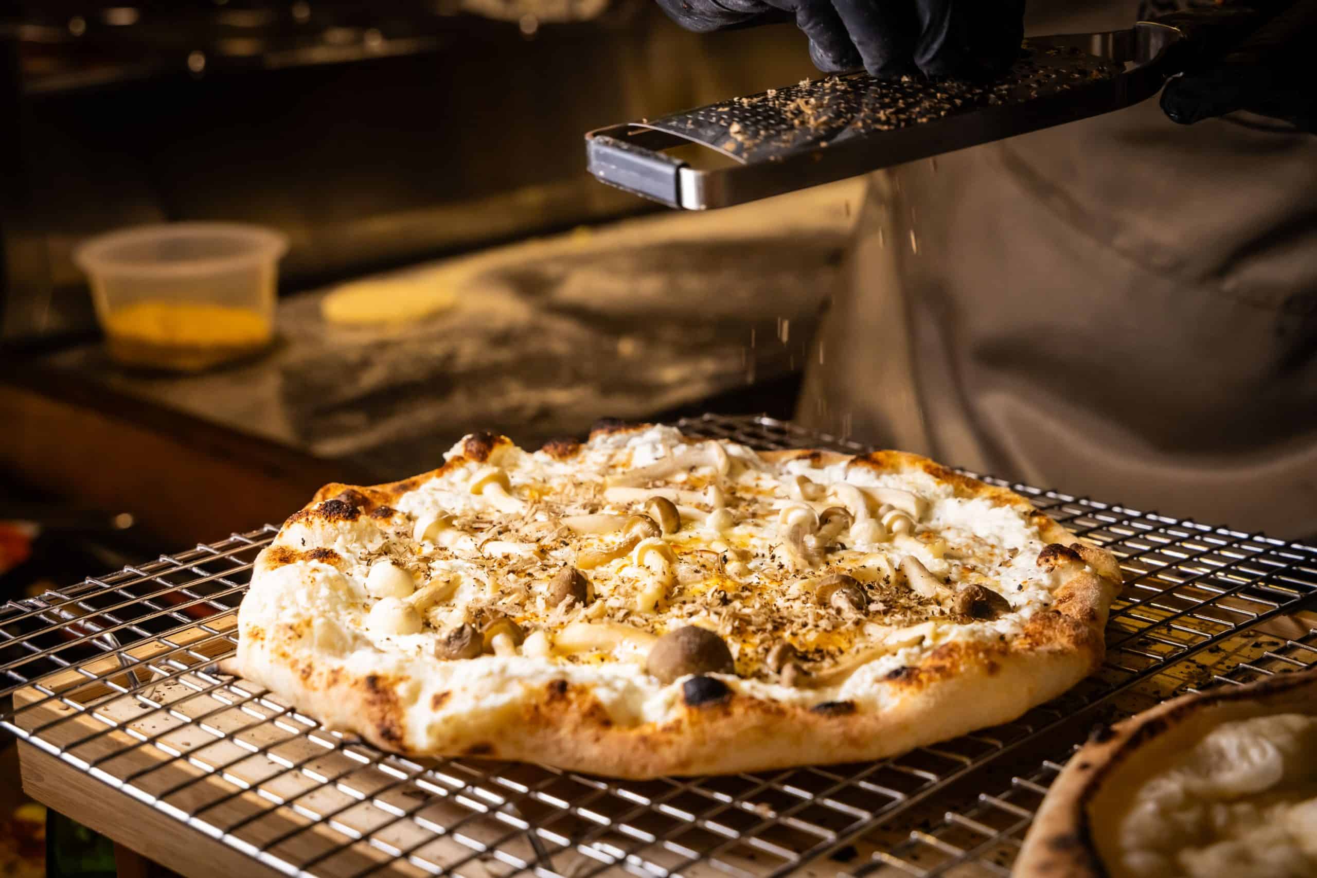 Eine Person reibt frischen Trüffel über eine mit Pilzen belegte Pizza beim Trüffelfestival Graz 2026.